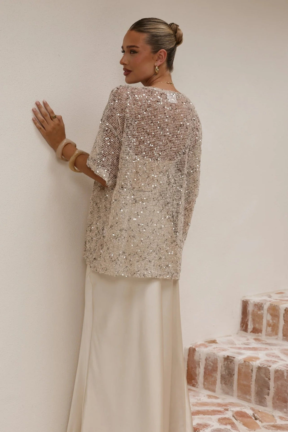 Woman wearing a sparkling top and white skirt on a staircase.