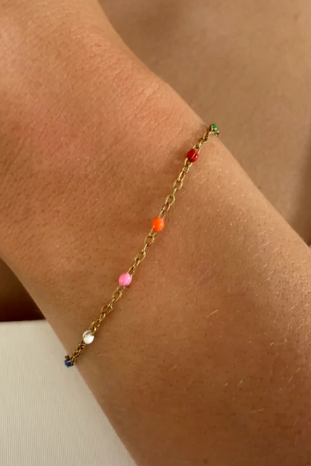 Gold bracelet with colorful beads on a wrist against a neutral background