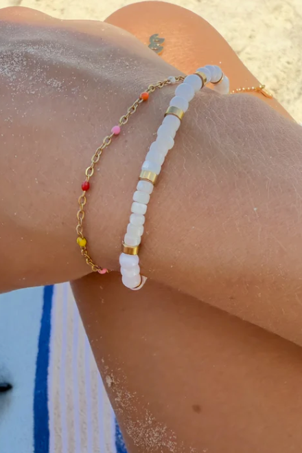 Close-up of a person's wrist wearing two bracelets on a beach.