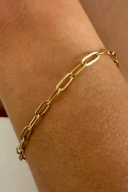 Gold chain bracelet on a wrist against a neutral background