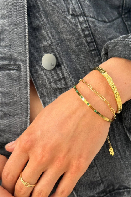 Person wearing gold bracelets on a gray denim jacket background