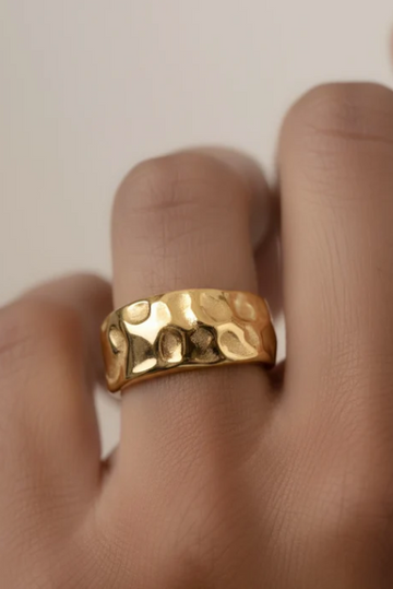 Gold ring on a finger against a neutral background