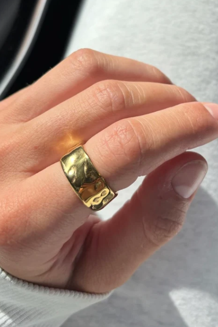 Gold ring on a finger against a neutral background