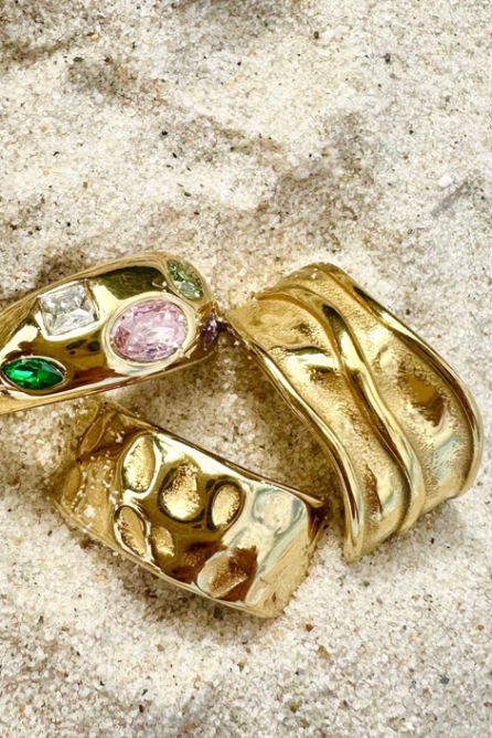 Two gold rings with gemstones on a sandy surface