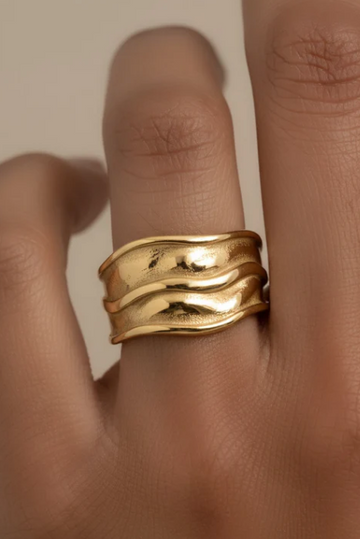 Gold ring on a finger against a neutral background