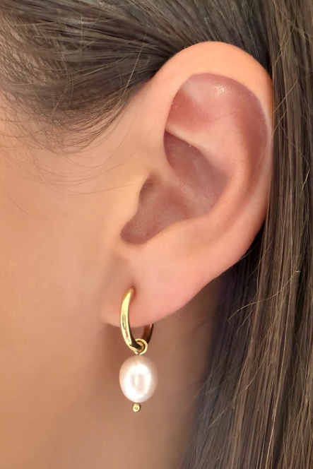 Gold hoop earring with a pearl pendant worn by a person.