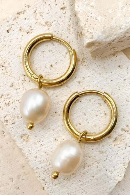 Gold hoop earring with a pearl pendant worn by a person.
