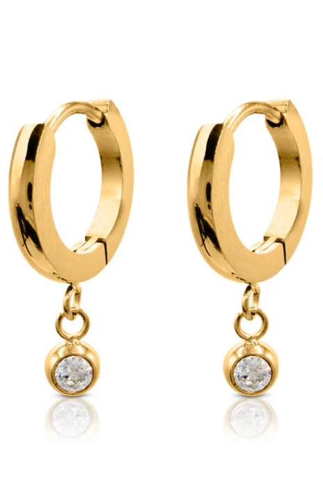 Gold hoop earring with a small round pendant worn by a person with blonde hair.