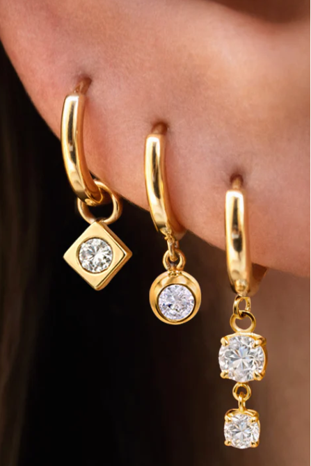 Gold hoop earrings with embedded crystals worn by a person.