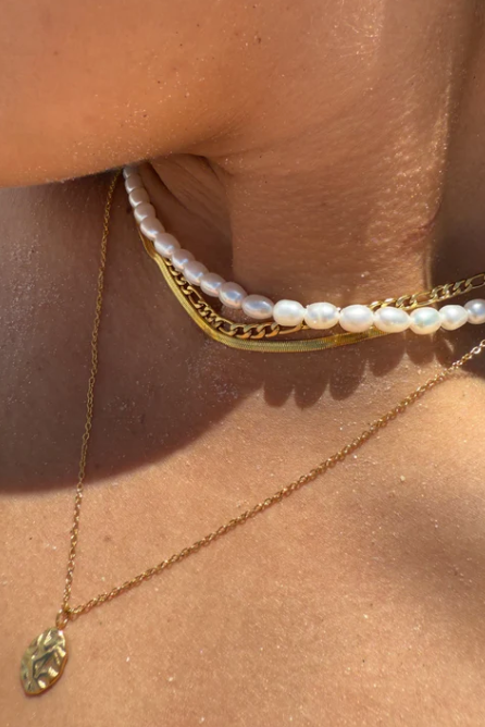 Close-up of a person wearing a gold necklace and pearl bracelet on a sunlit skin background