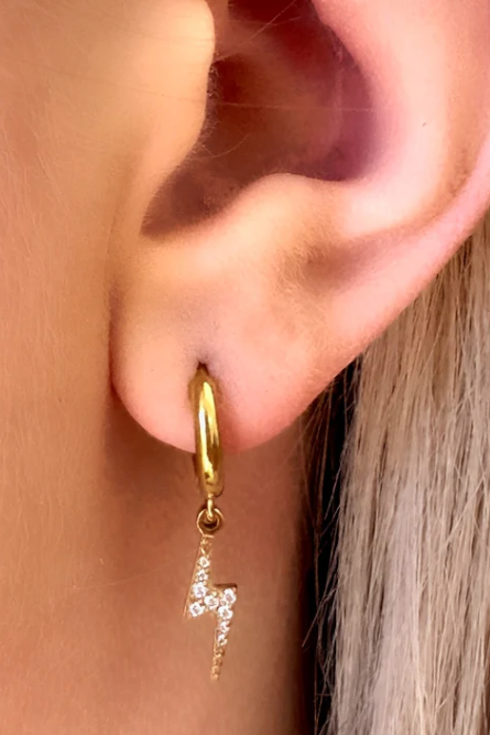 Gold hoop earring with a small diamond pendant worn by a person with blonde hair.