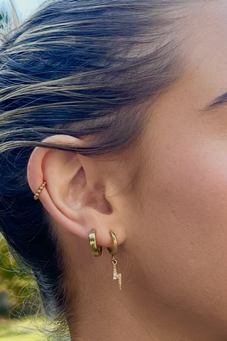 Close-up of a person wearing gold hoop earrings with a blurred natural background