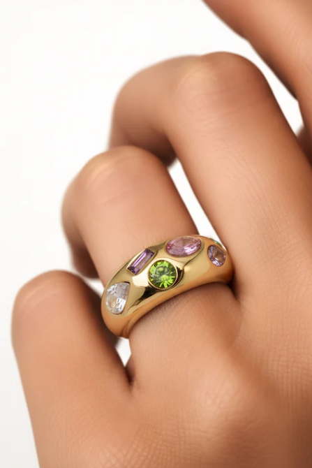 Gold ring with colorful gemstones on a hand against a white background