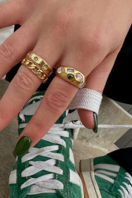 Hand with green nail polish wearing gold rings on a green sneaker.