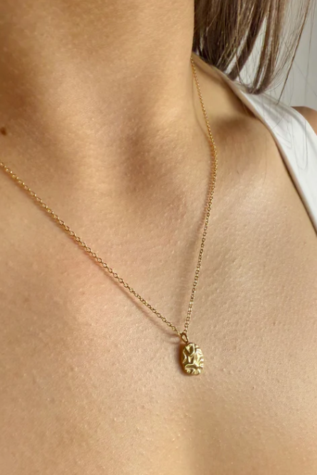 Gold necklace with a pendant on a person wearing a white top.