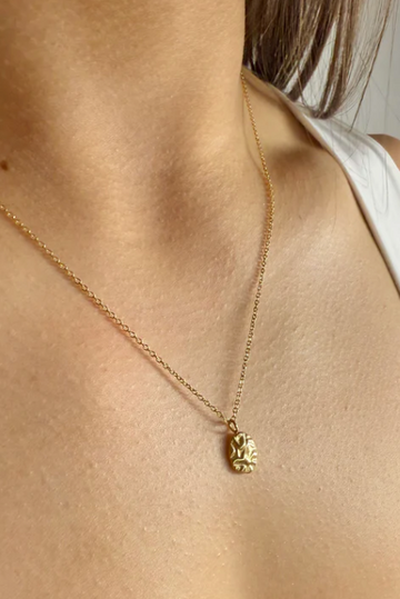 Gold necklace with a pendant on a person wearing a white top.