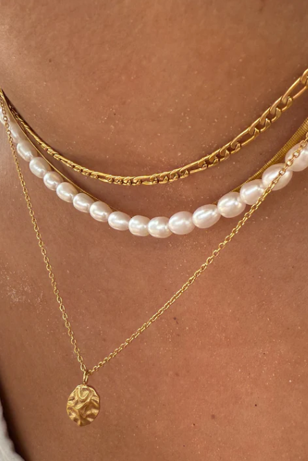 Close-up of a person wearing multiple necklaces including gold chains and a pearl necklace.