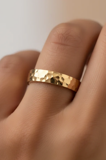 Gold ring on a finger against a neutral background