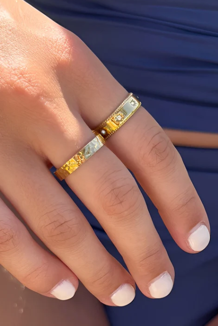 Close-up of a hand wearing two gold rings with a blue background