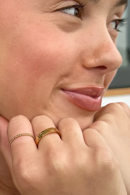 Close-up of a woman with a gold ring on her finger, looking away from the camera.