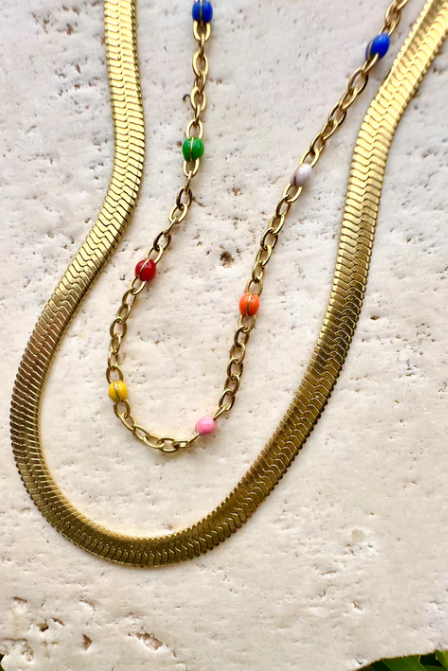 Three gold necklaces with colorful beads on a textured stone surface.
