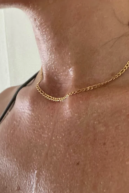 Gold chain necklace on a person's neck with a neutral background