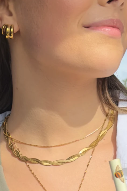Close-up of a woman wearing gold necklaces and earrings outdoors.