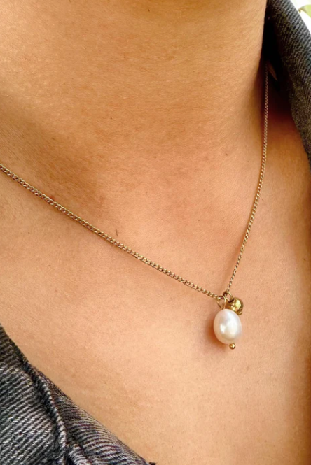 Necklace with a pearl pendant worn by a person against a denim background