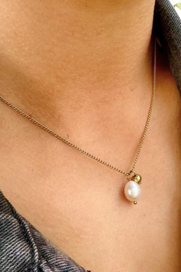 Necklace with a pearl pendant worn by a person against a denim background