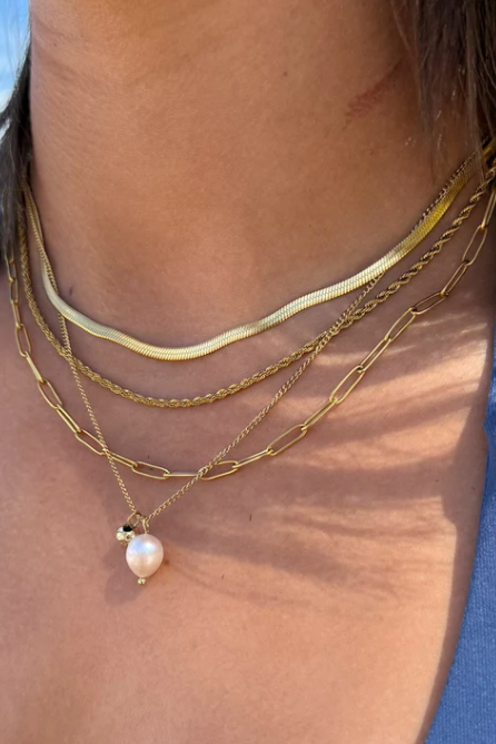 Close-up of a person wearing multiple gold necklaces with a pearl pendant against a blue sky.