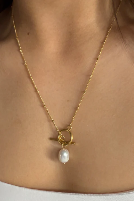 Gold necklace with a pendant featuring a pearl on a person wearing a white top.