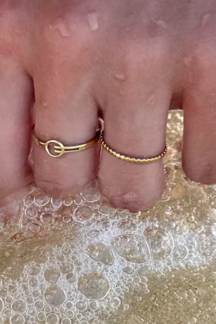 Hand with gold rings in water, possibly at a beach