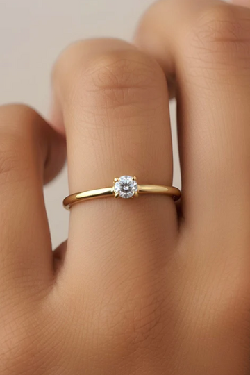 Gold ring with a diamond on a person's finger against a neutral background