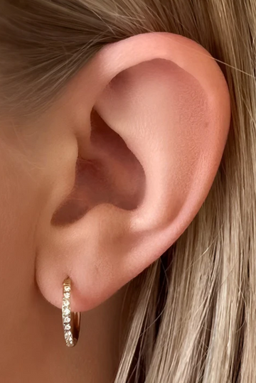 Close-up of an ear wearing a gold hoop earring with small diamonds.