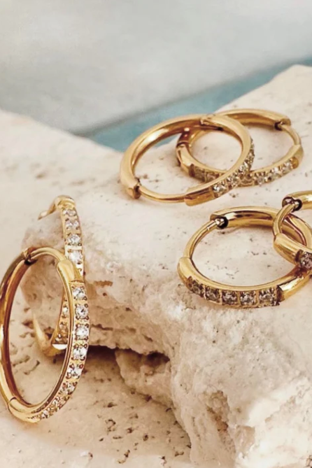 Gold hoop earrings with diamond accents on a textured stone surface
