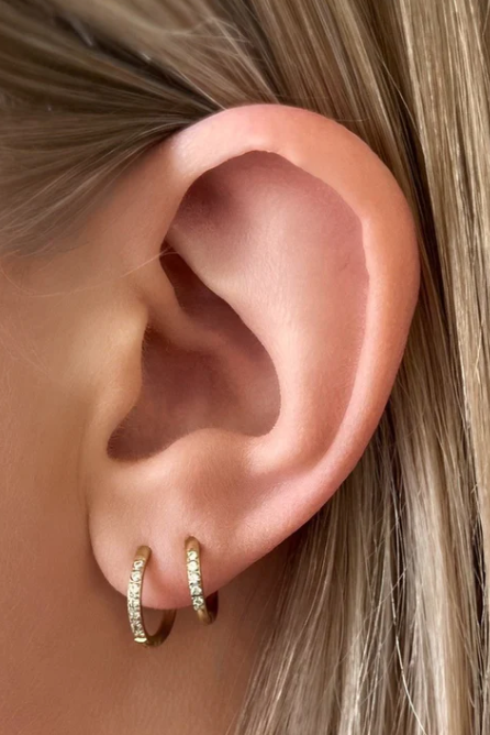 Close-up of an ear wearing gold hoop earrings with small diamonds.