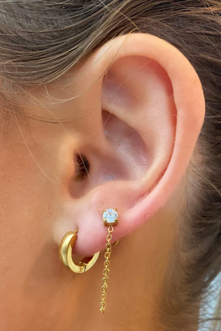 Close-up of an ear wearing gold hoop earrings with a central gemstone.