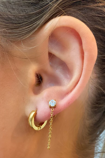 Close-up of an ear wearing gold hoop earrings with a central gemstone.