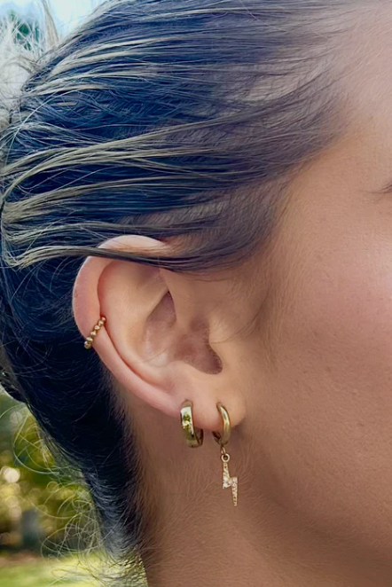 Close-up of a person's ear with gold hoop earrings outdoors