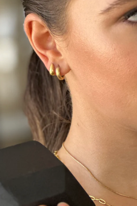 Close-up of a woman wearing gold earrings and a necklace, holding a black object.
