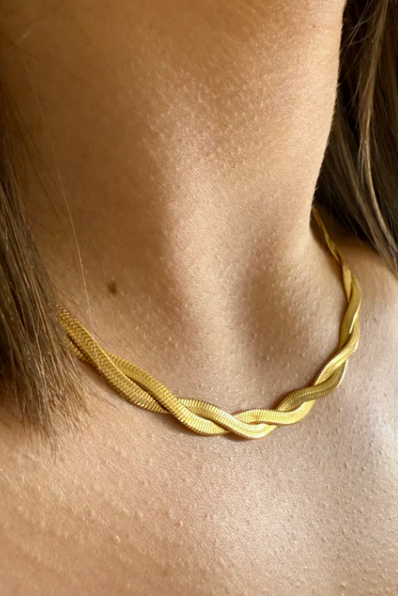 Gold necklace on a person's neck with a neutral background