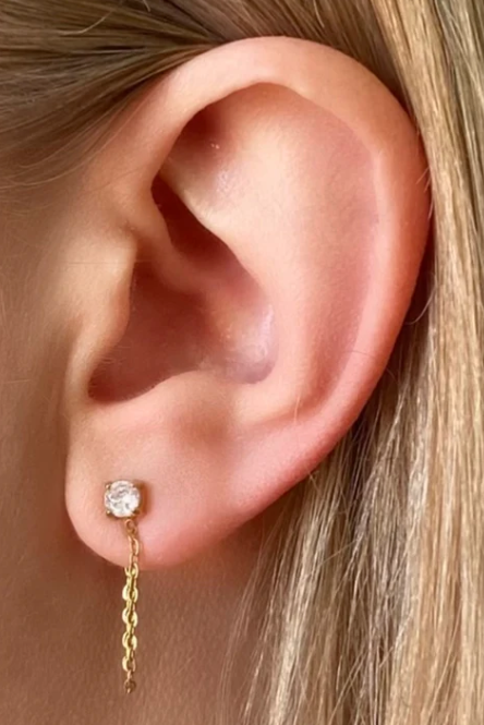 Close-up of an ear wearing a gold earring with a clear gemstone.