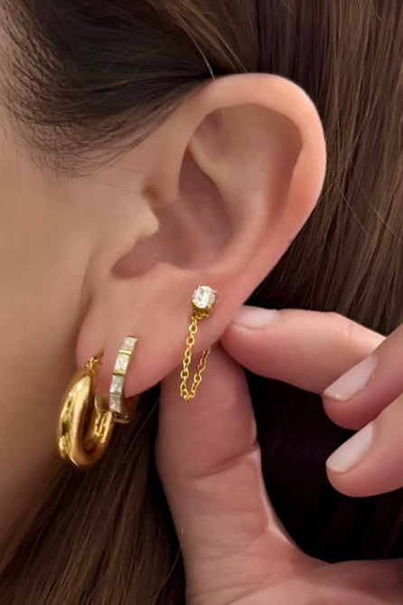 Close-up of a person wearing gold hoop earrings with a hand adjusting them.