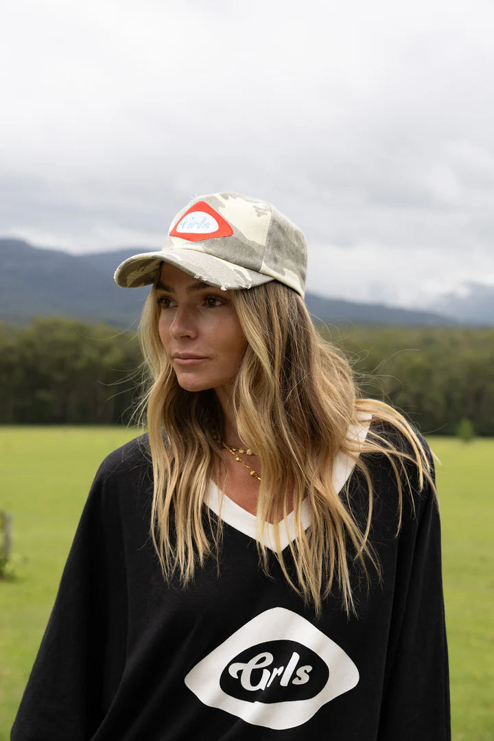 Woman wearing a cap and black sweater with 'GRLS' logo in an outdoor setting