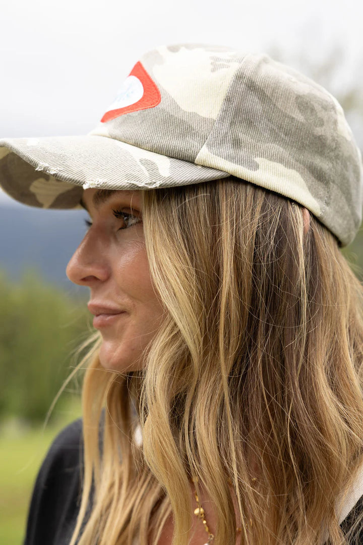 Woman wearing a camouflage cap with a red logo outdoors