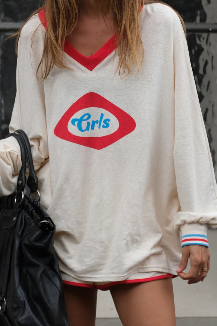 Person wearing a white sweatshirt with a red and blue logo, holding a black bag.