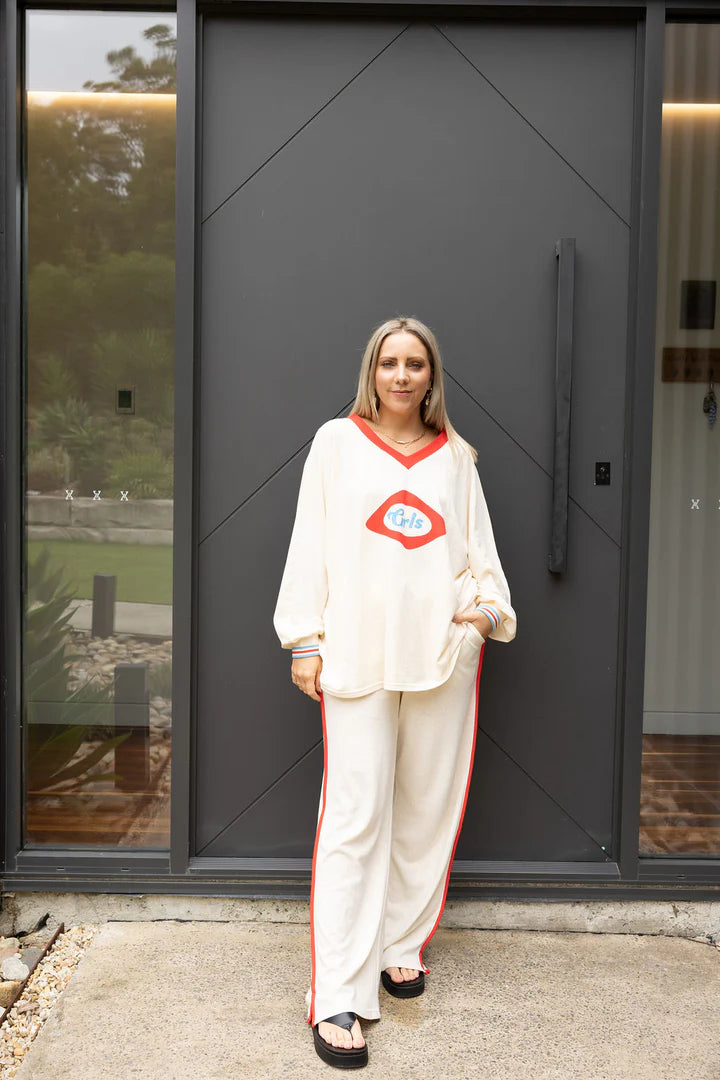 Woman in a white outfit with red accents standing in front of a modern building entrance.