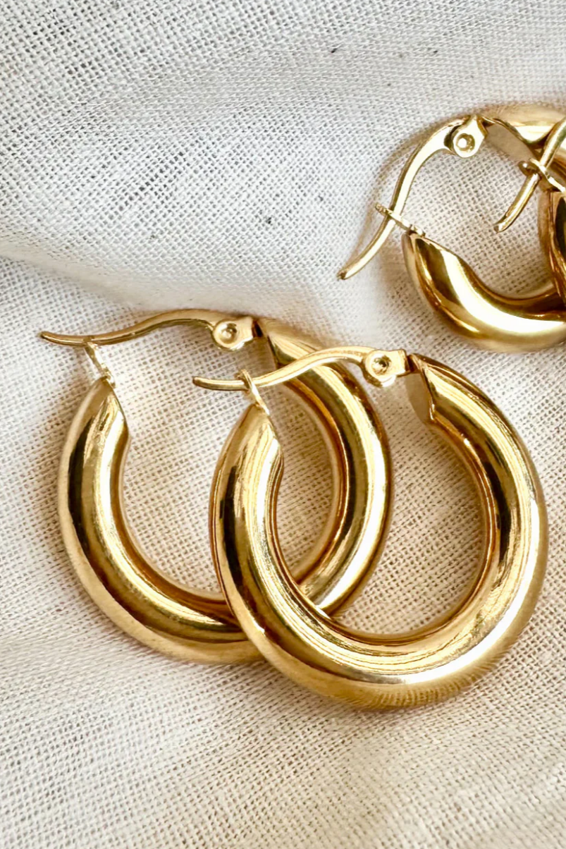 Pair of gold hoop earrings on a beige fabric background